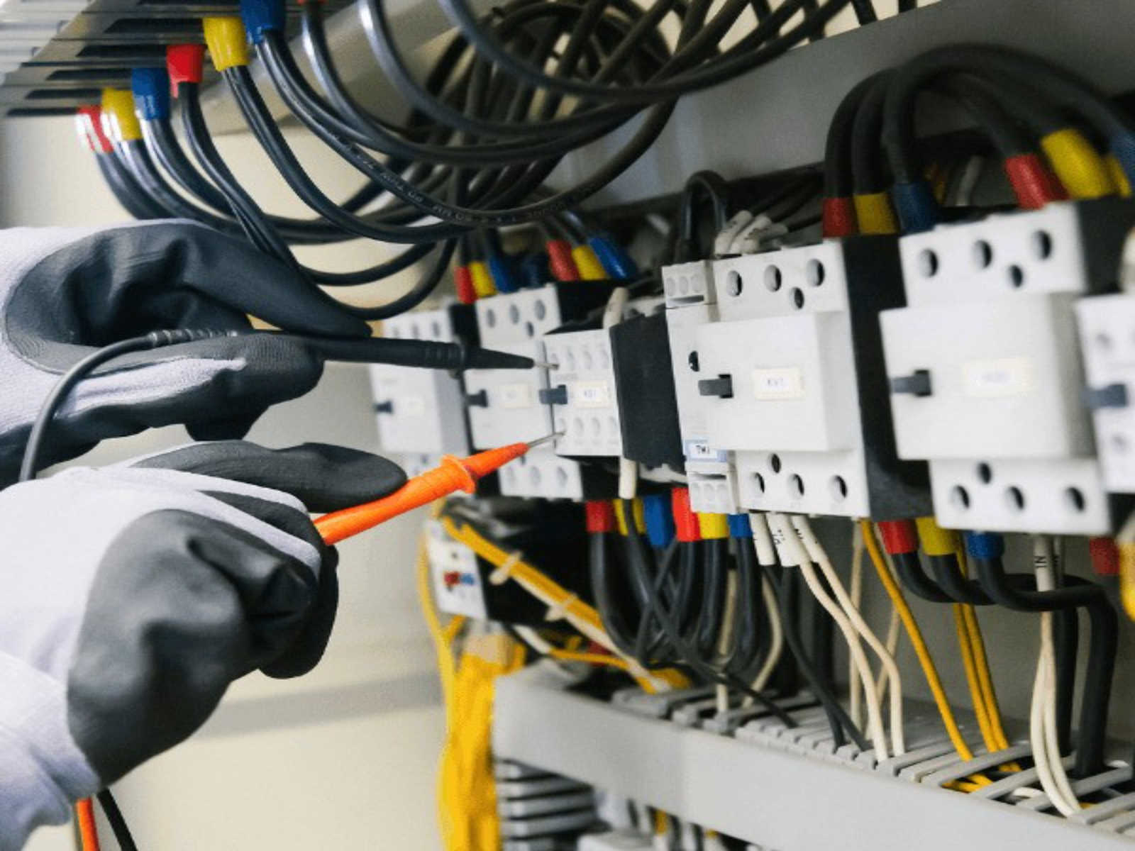 Gloved hands taking a reading with a test probe at a distribution board.